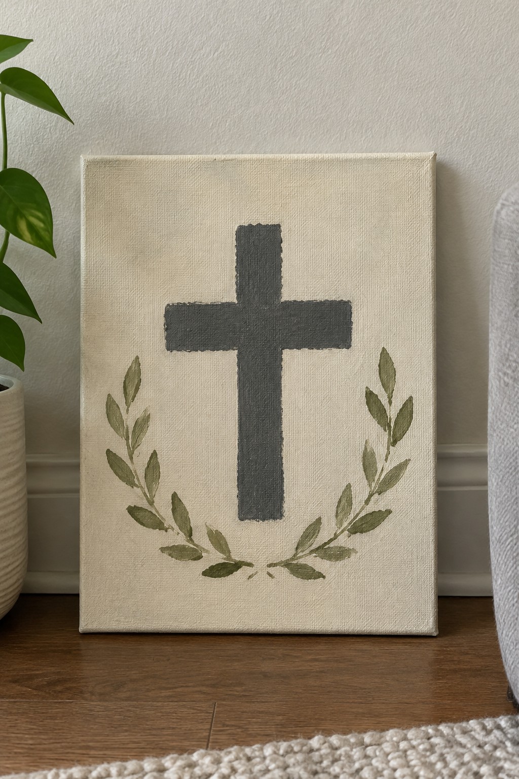 Canvas with black cross above green leaf wreath on wooden floor