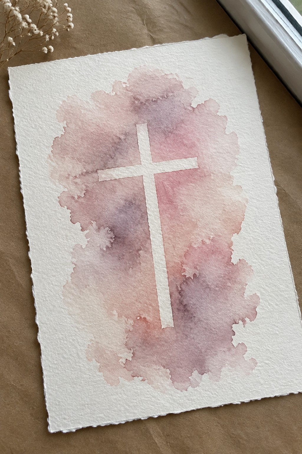 Soft pink purple watercolor wash with white cross and dried flowers on paper