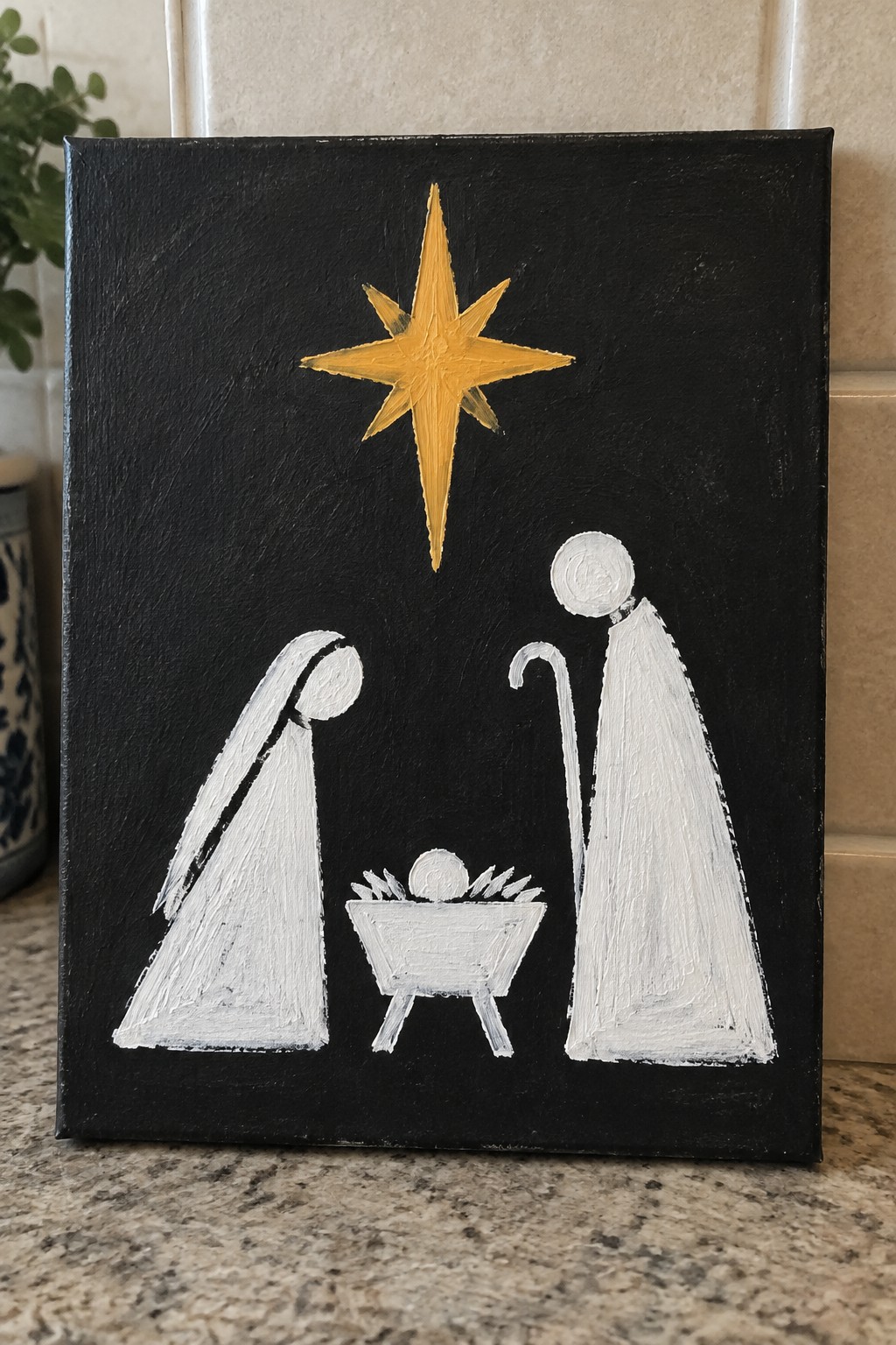 Minimalist white nativity figures with golden star above manger on black canvas.