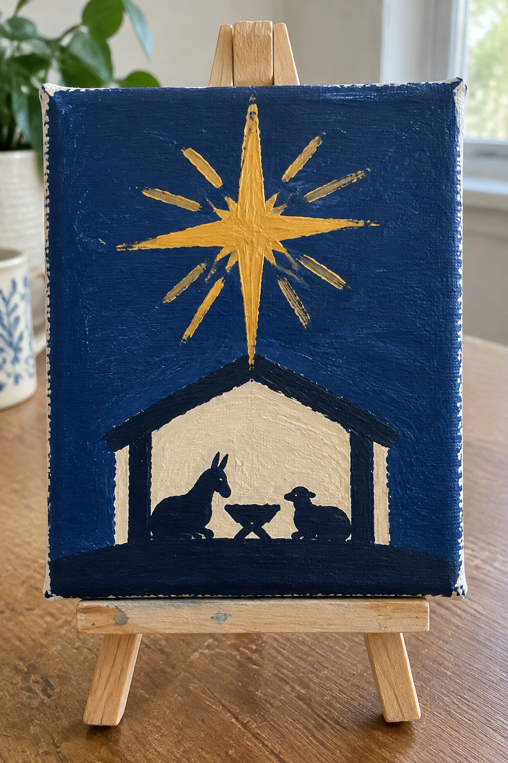 Nativity painting on easel shows golden star above donkey and lamb in stable