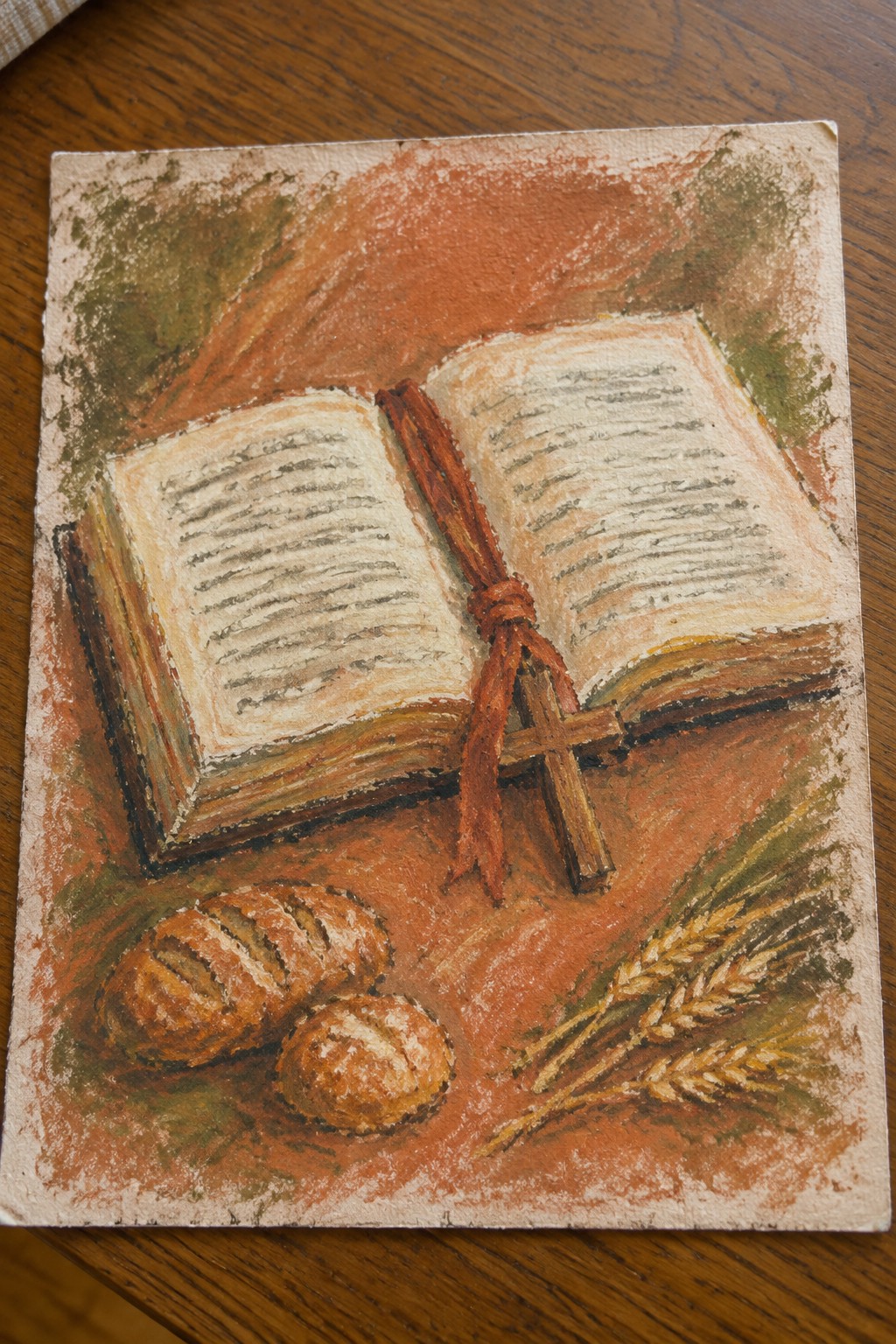 Open book with red ribbon and cross beside bread rolls and wheat on red background