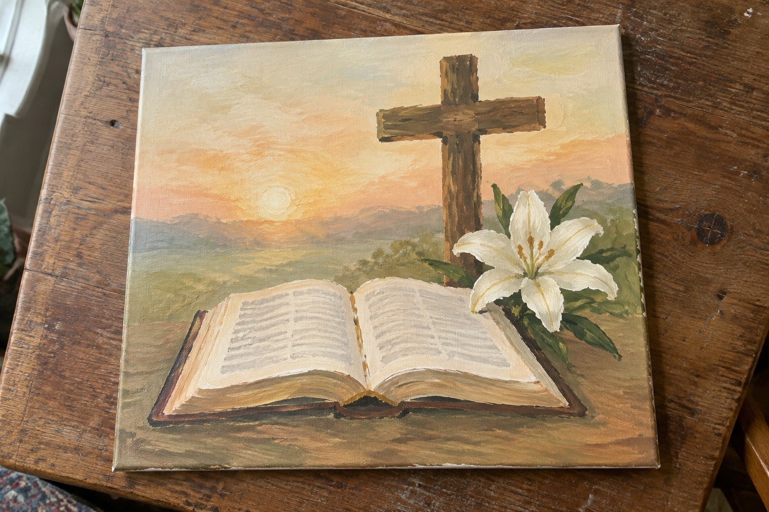 Open Bible, wooden cross and white lily against orange sunset over green hills.