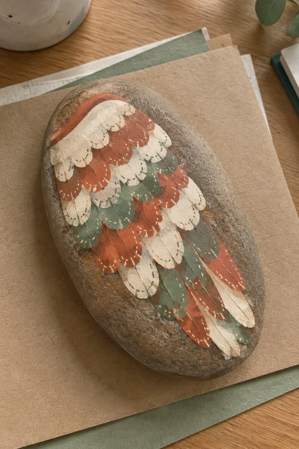 Oval stone painted with scalloped wing feathers in rust, cream, and green tones