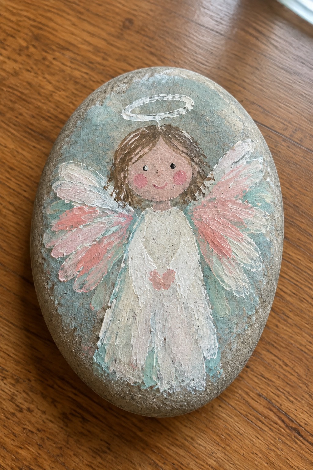 Hand-painted angel on oval stone with white dress, pink wings, and halo