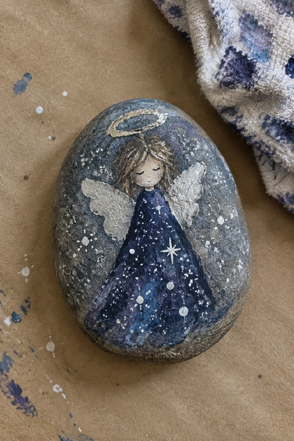 Painted rock angel in starry blue dress with halo, silver wings, and stars