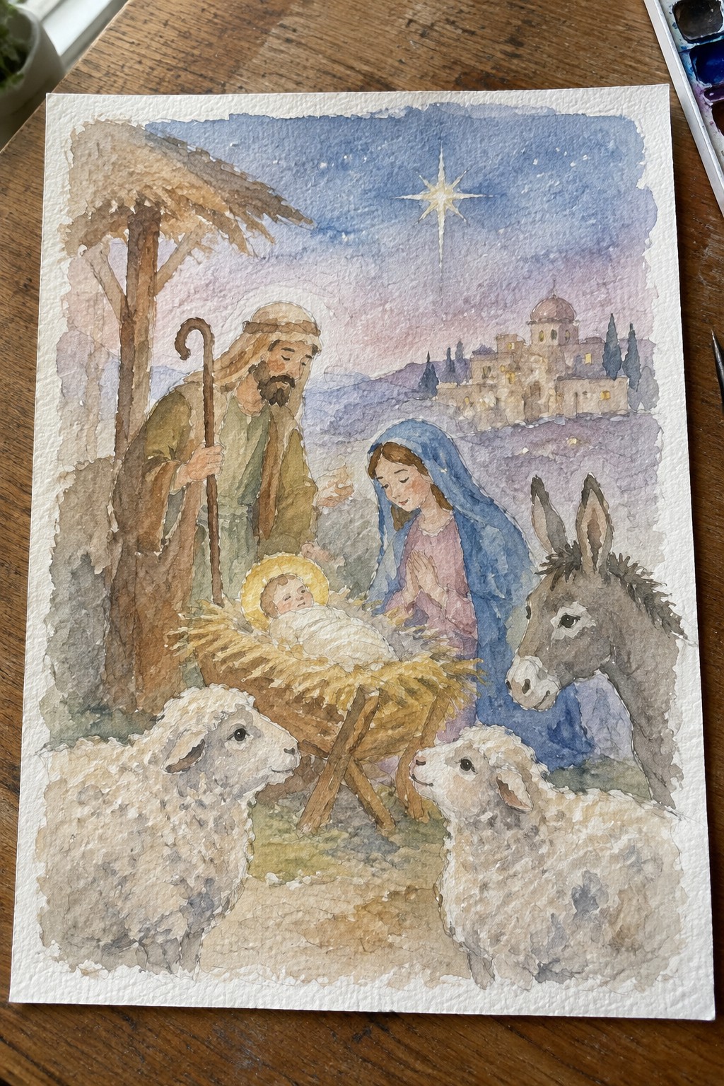 Watercolor nativity with Mary in blue veil, Joseph with staff, manger, sheep, donkey and star