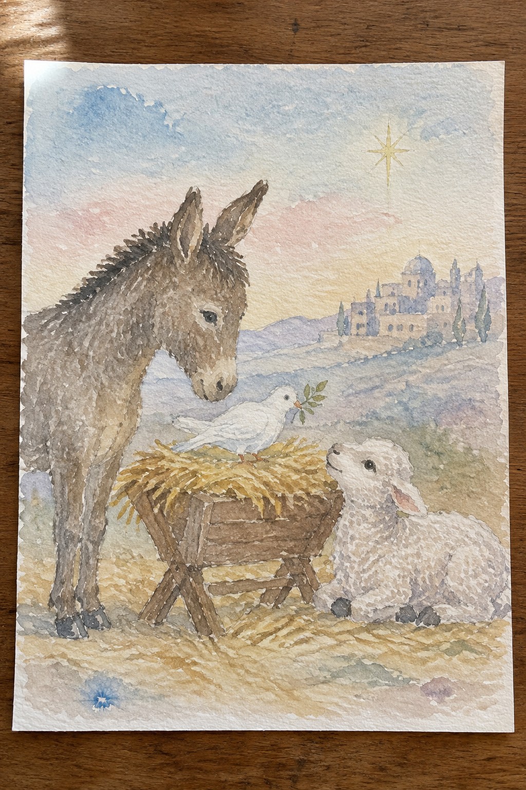 Watercolor nativity with donkey, lamb, dove on manger, and star over town.