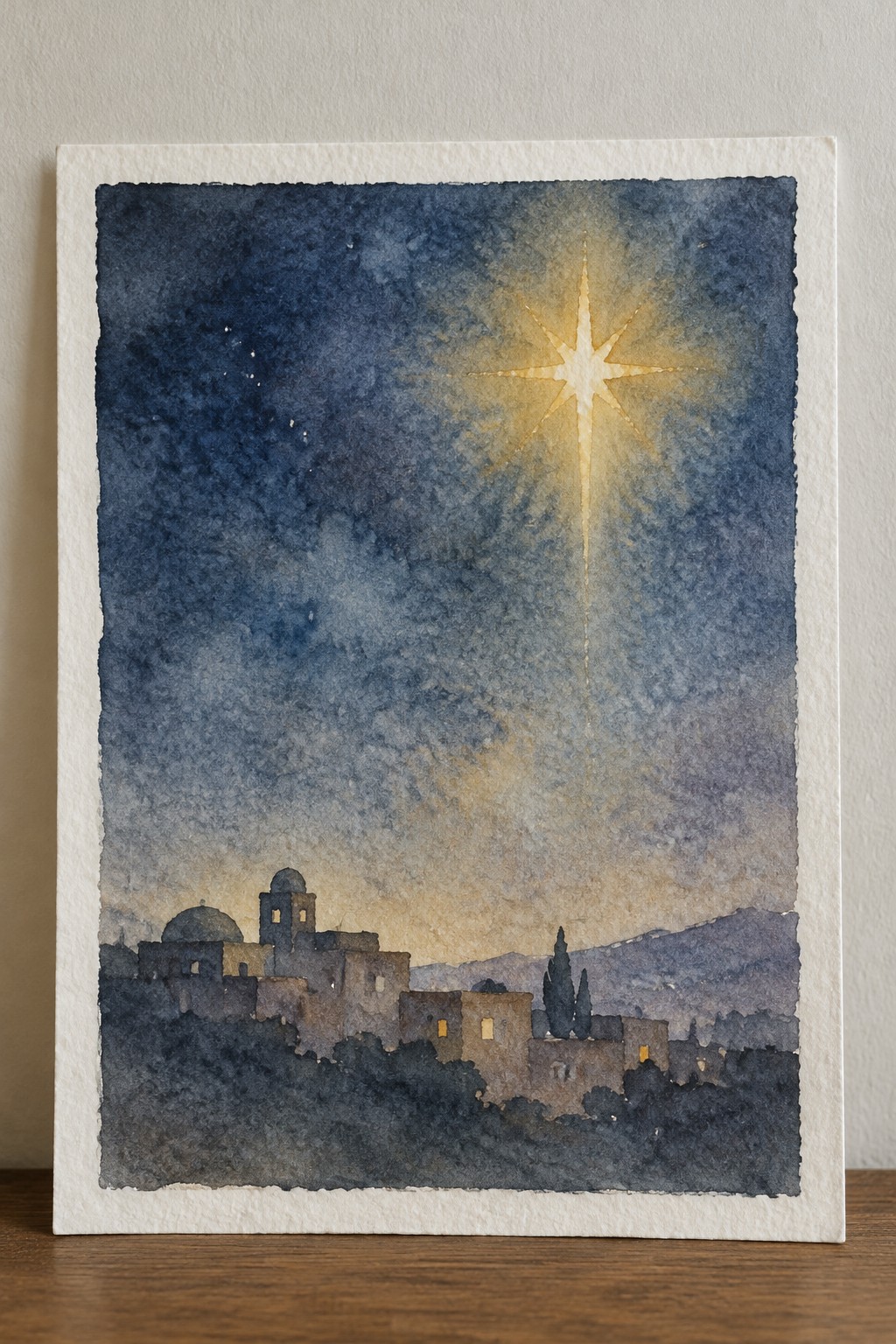 Watercolor night scene of a radiant star glowing above a silhouetted town with domes and hills.