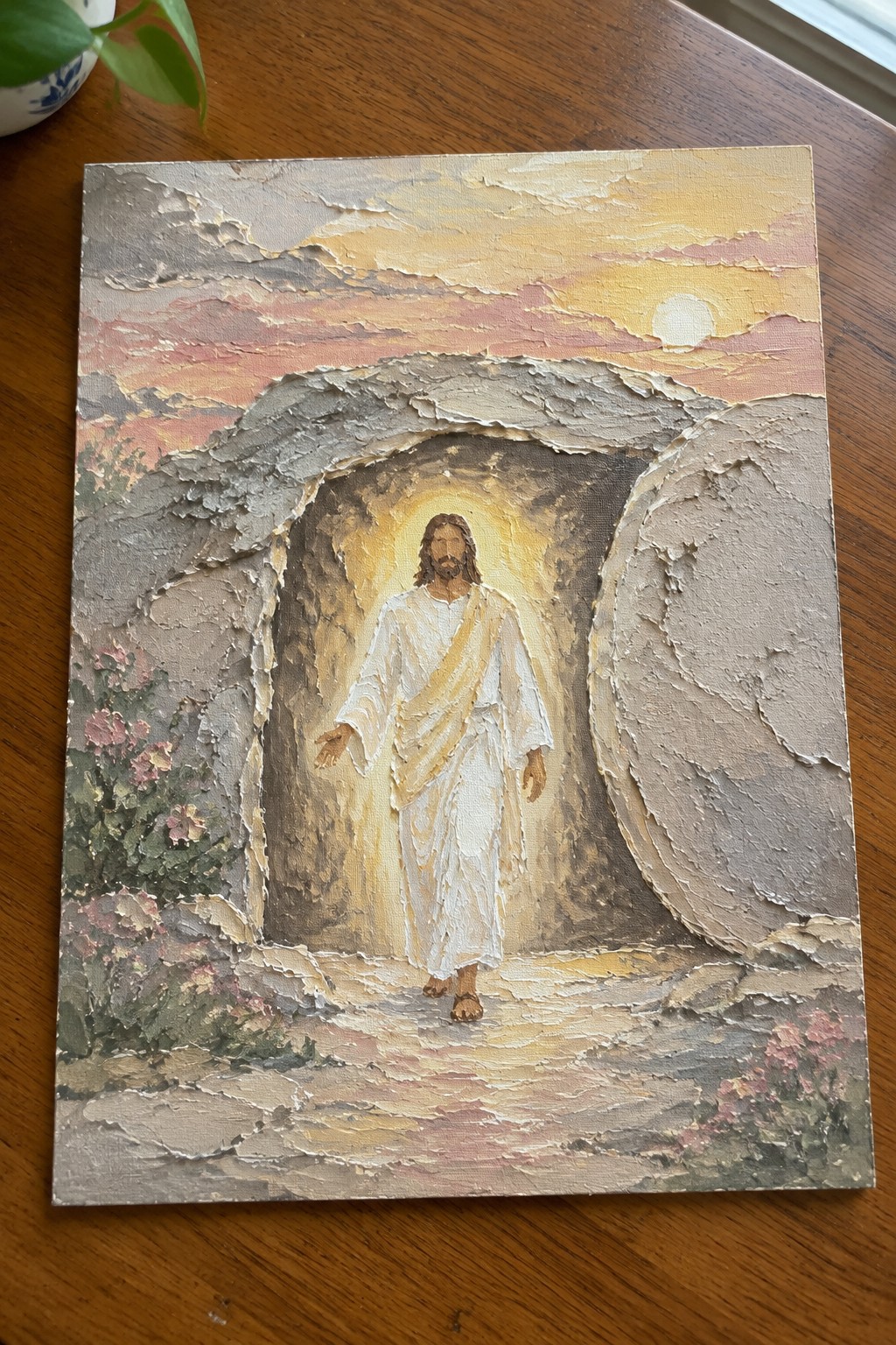 Jesus in white robes with gold sash emerging from glowing stone tomb at sunrise