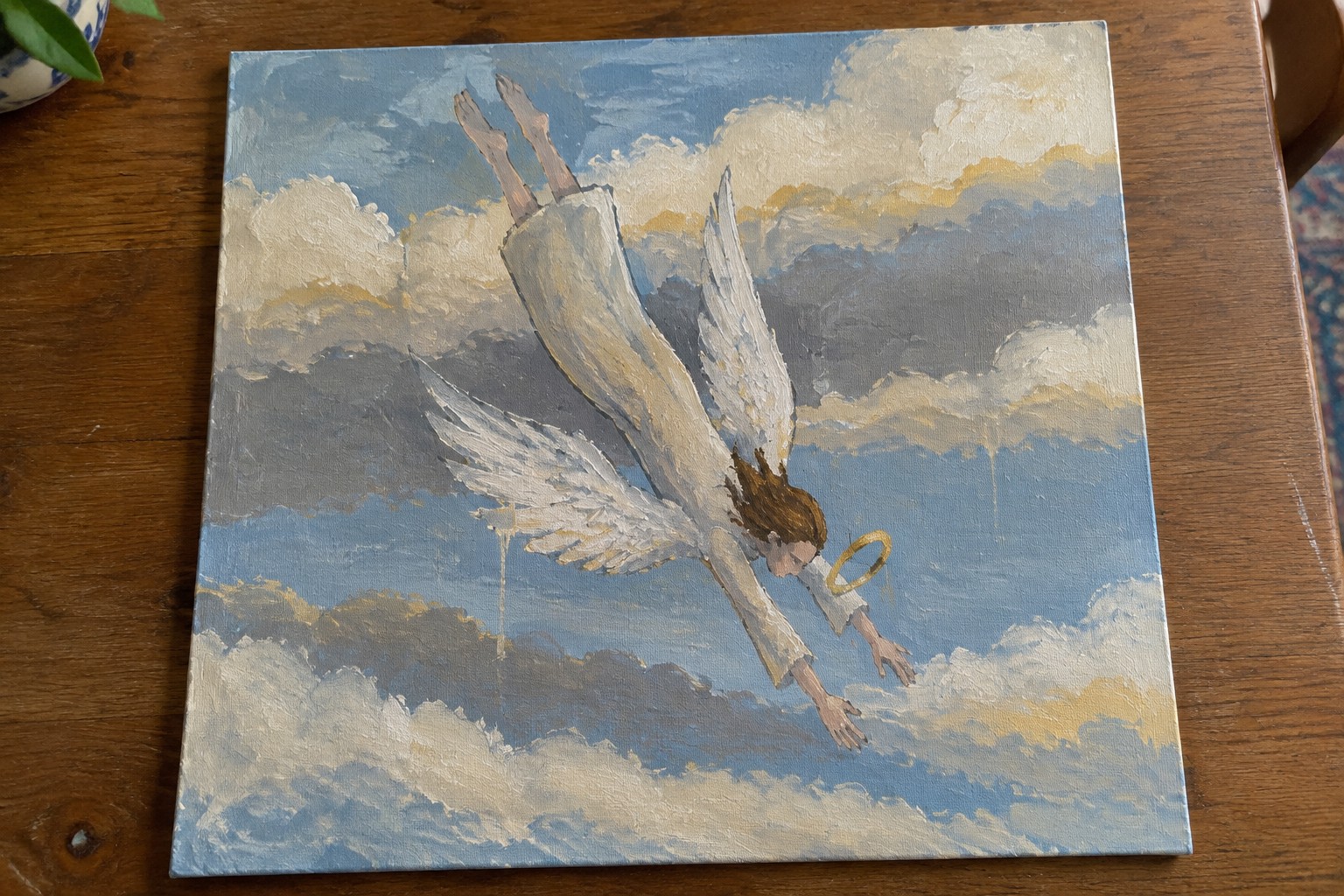 Falling angel in white robe with spread wings and slipping halo amid blue clouds
