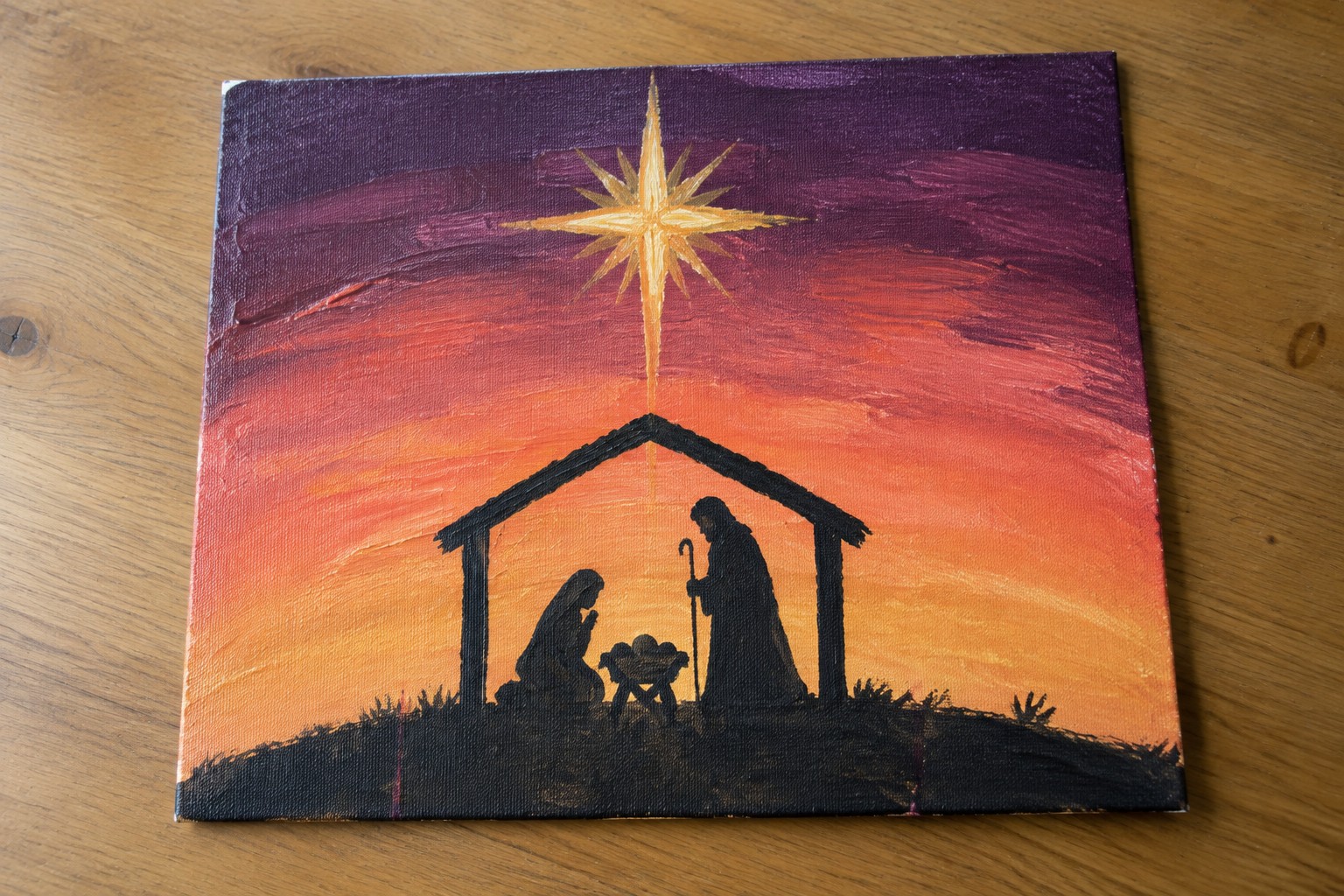 Canvas painting of black nativity silhouettes under golden star in orange-purple sky