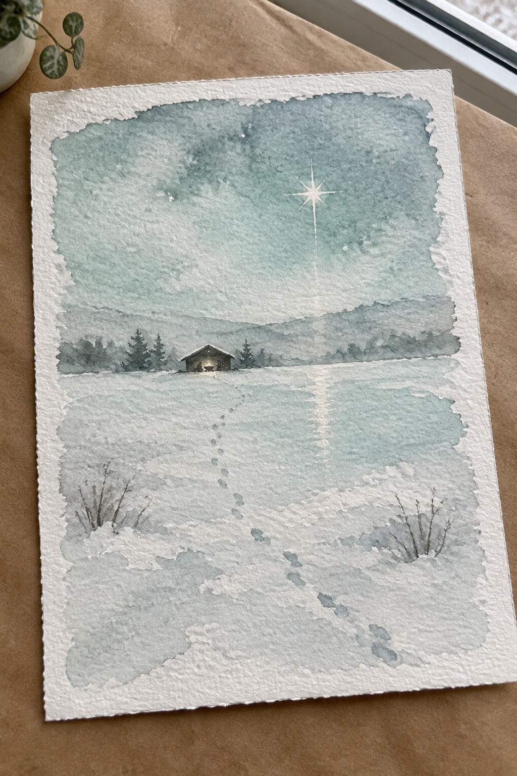 Watercolor of snowy field with footprints leading to lit cabin under bright star.
