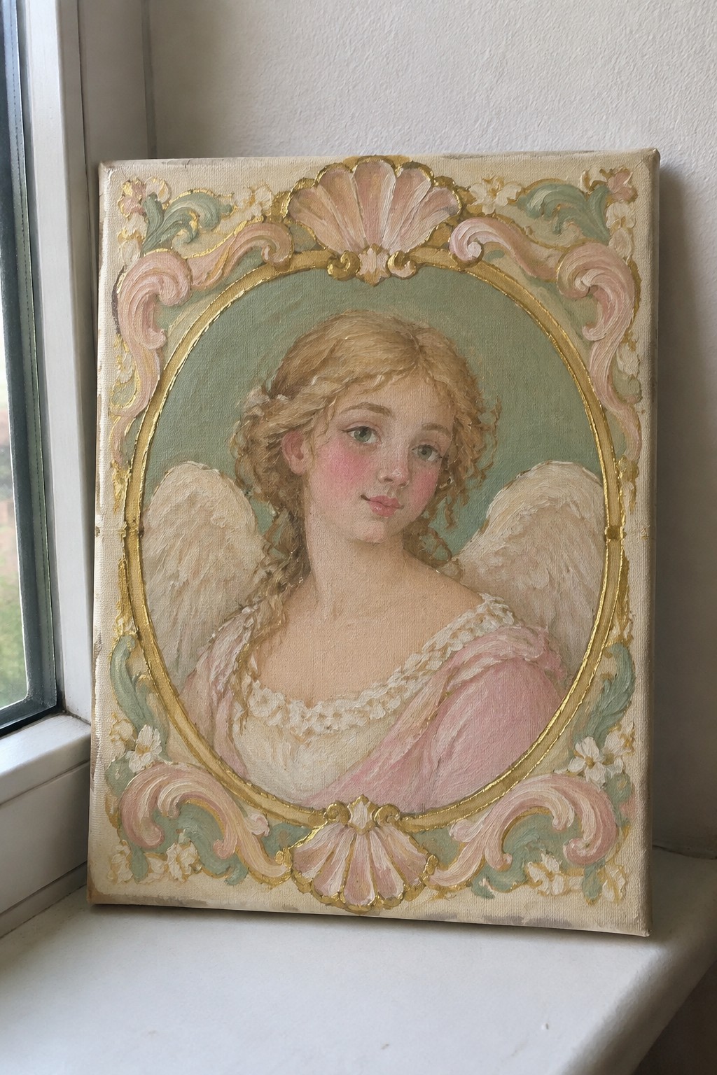 Ornate gold-framed portrait of blonde angel in pink dress on windowsill.