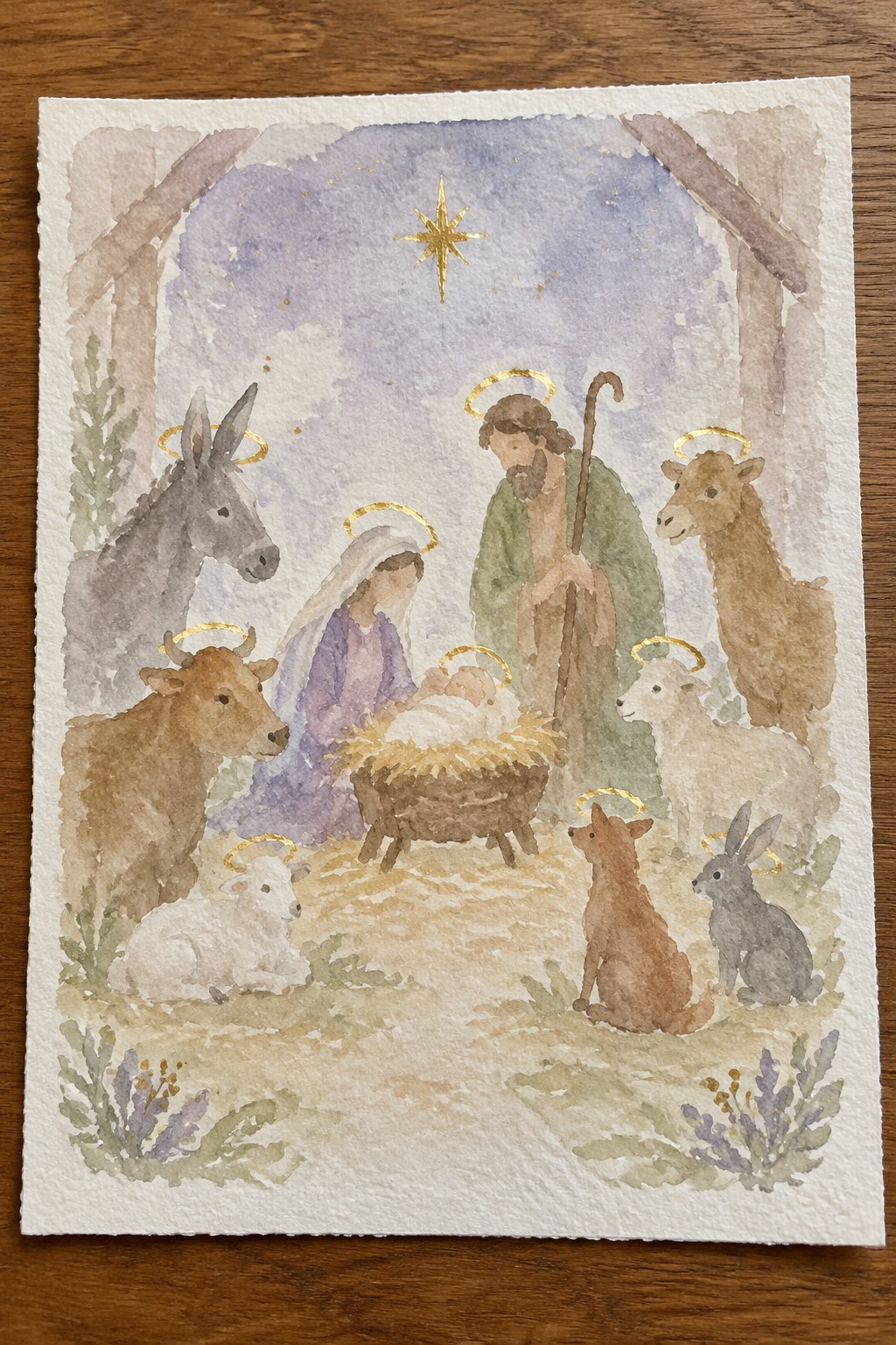 Watercolor nativity scene with haloed Mary, Joseph, baby Jesus and animals under golden star.