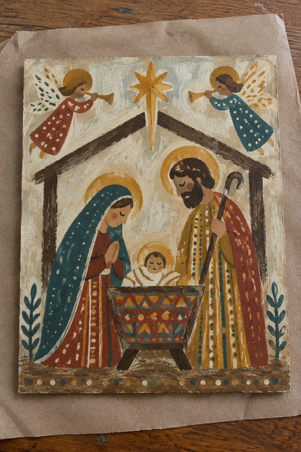 Folk art nativity with Mary in blue veil, robed Joseph, angels with trumpets, and manger.