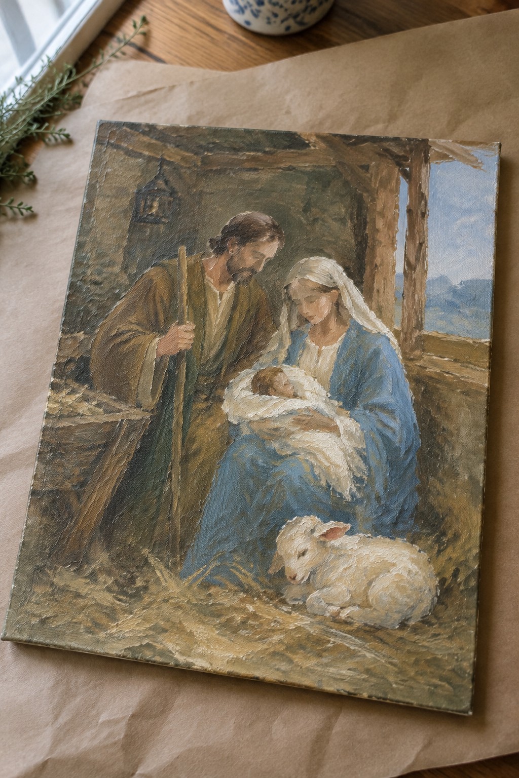 Oil painting of Mary in blue holding swaddled infant beside Joseph and white lamb in stable