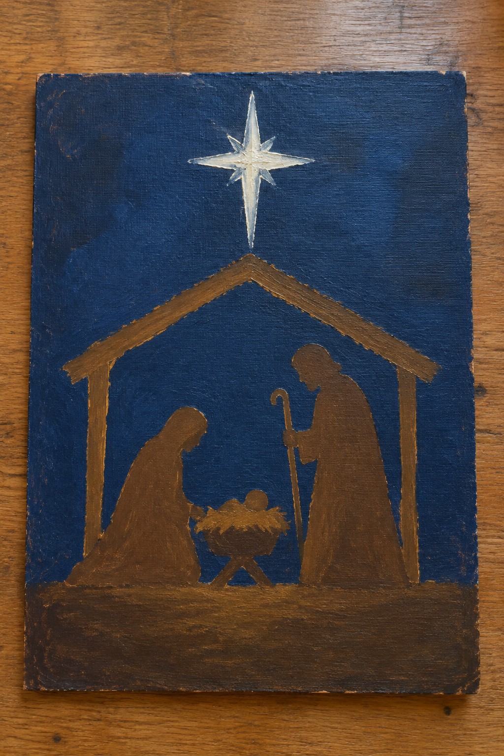 Nativity painting with robed Mary, Joseph with staff, manger, stable, and white star on blue.