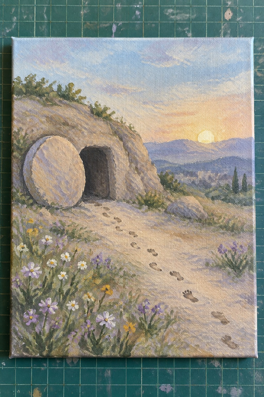 Sunset painting of empty rock tomb with round stone aside, footprints amid wildflowers.