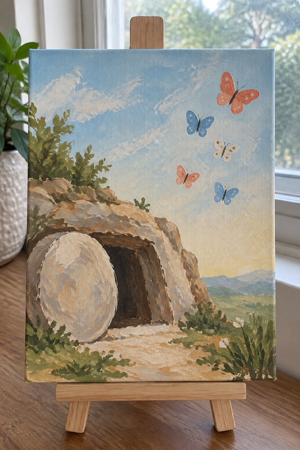 Painting on easel of empty tomb with rolled stone, butterflies, and landscape.