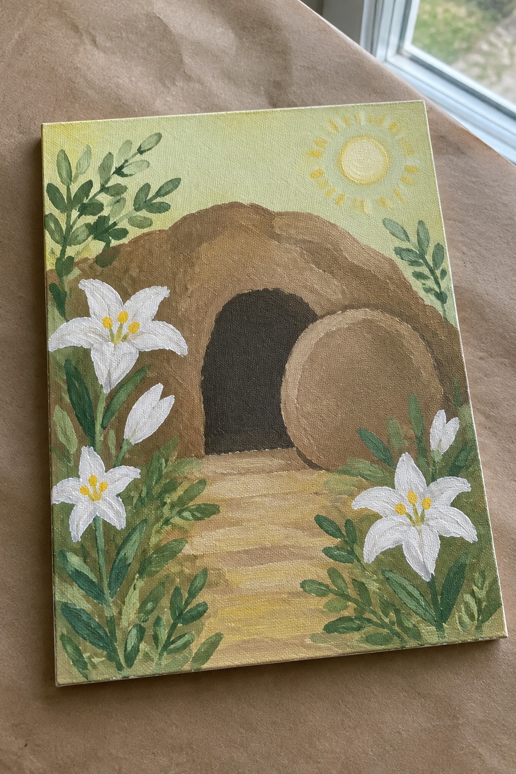 Empty tomb painting with rolled stone, white lilies, green foliage, and sun.