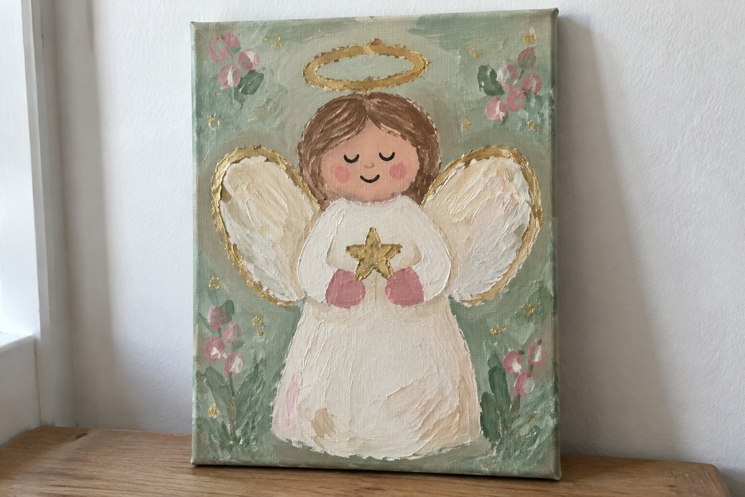 Whimsical canvas painting of angel with brown hair, halo, wings, holding star on green floral background.