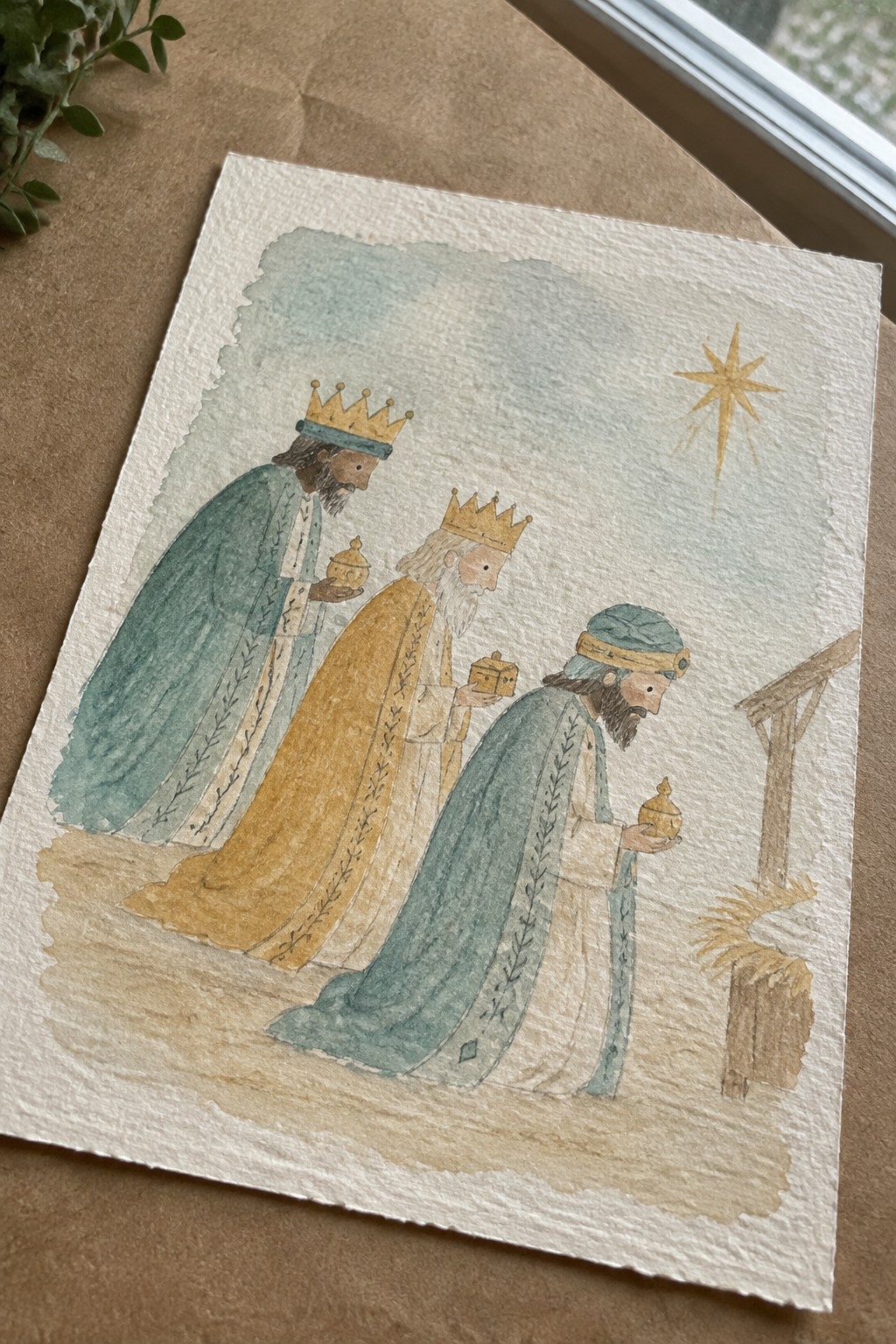 Three kings in teal and gold robes carry gifts toward a stable under a shining star