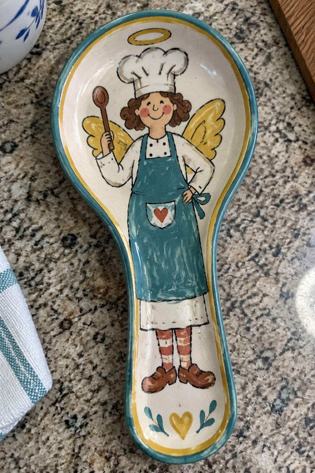 Ceramic spoon rest with hand-painted chef angel in teal apron, yellow wings, and halo