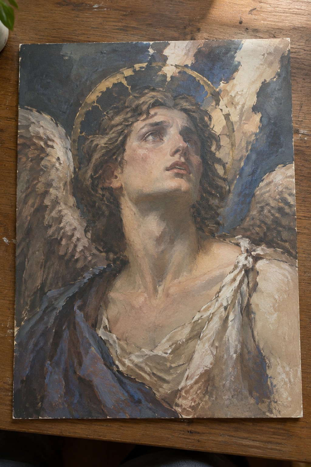 Winged angel with curly hair and golden halo gazes upward in tattered white drapery