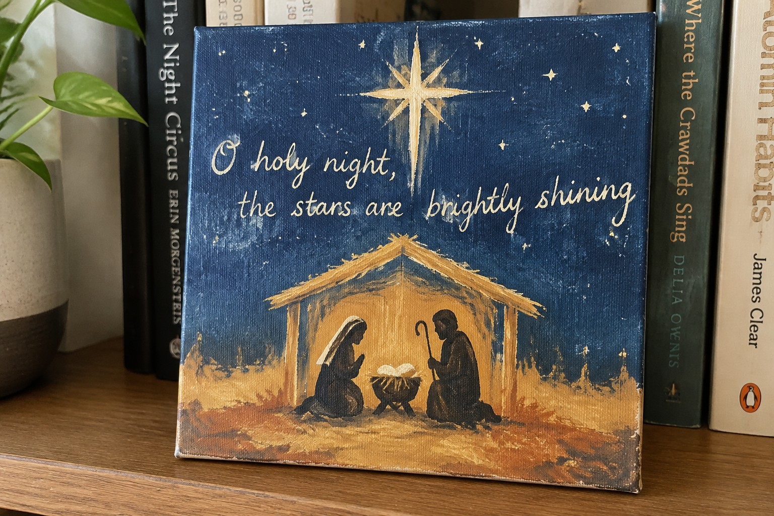 Painted canvas with a nativity scene under a large golden star and the words "O holy night, the stars are brightly shining" on a dark blue background.