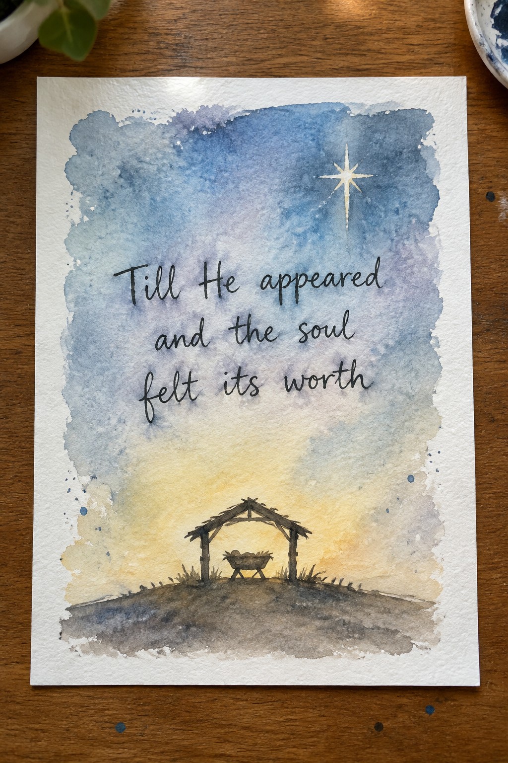 Watercolor nativity with manger, bright star, and cursive text on blue-yellow sky