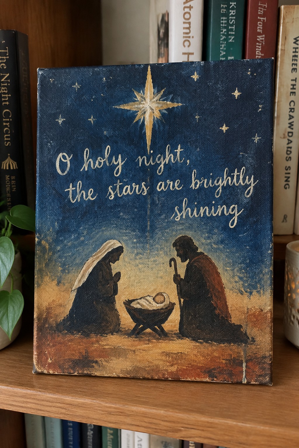 Painted canvas with a nativity scene under a large golden star and the words 