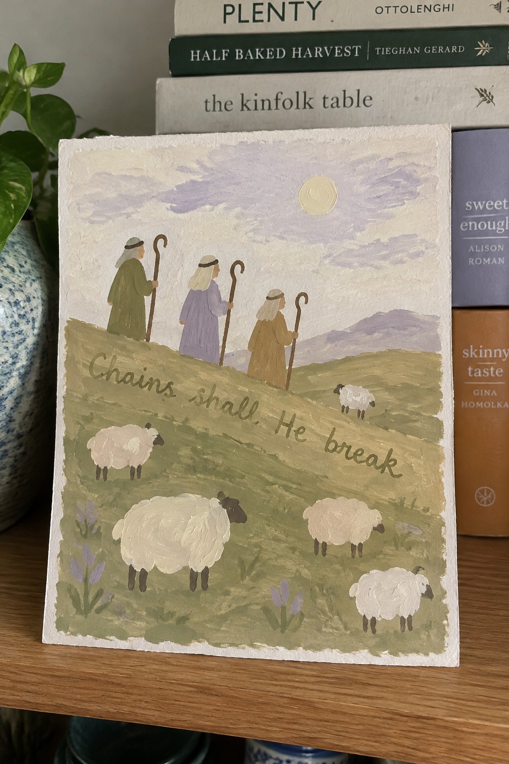 Three robed shepherds with crooks among sheep on green hill with painted text
