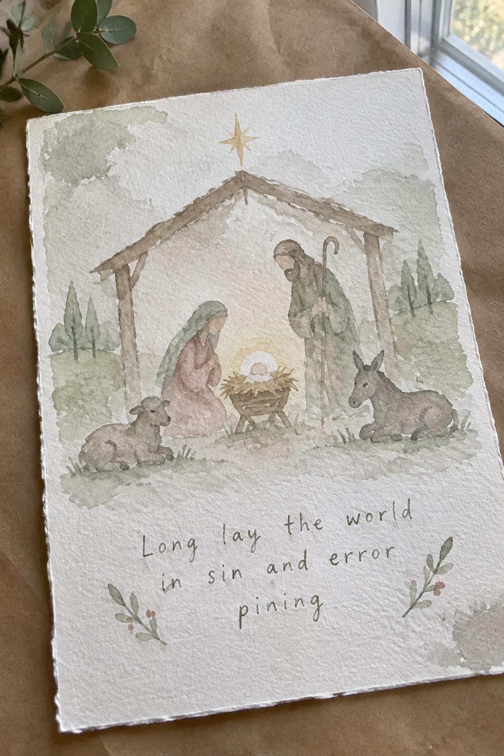 Watercolor nativity with Mary in pink dress, Joseph, manger, donkey, lamb, star above stable