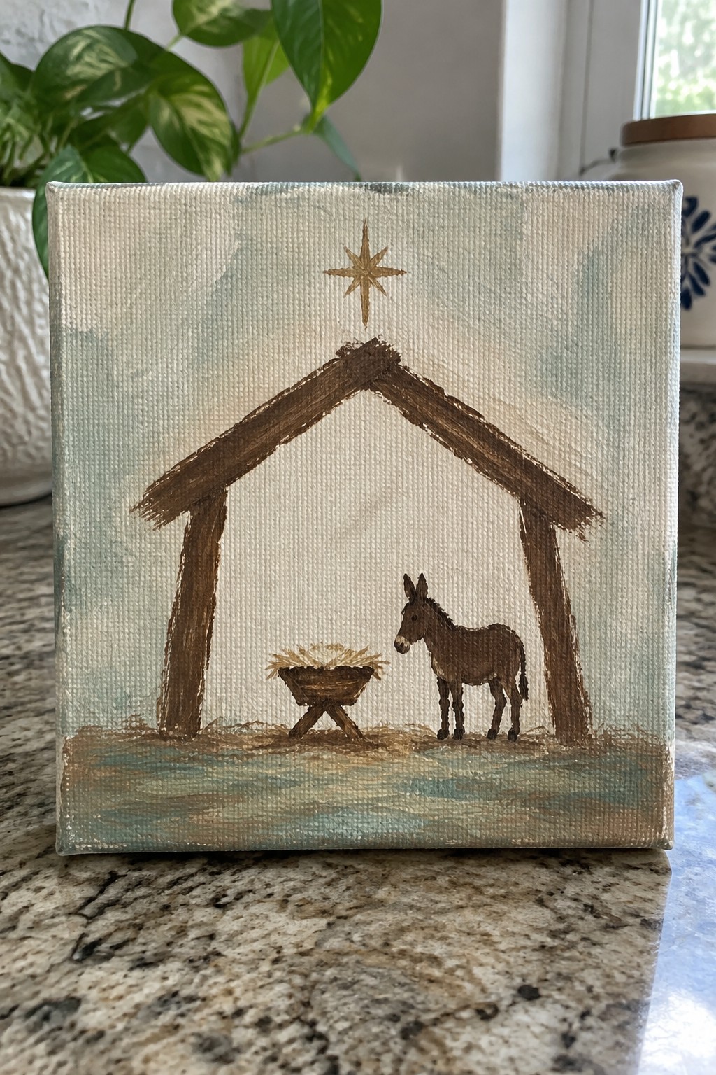 Small canvas painting of nativity stable, golden star, manger, and brown donkey.