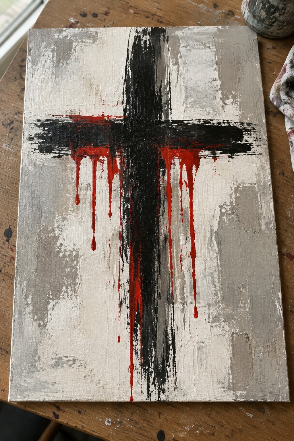 Abstract painting of black cross with red drips on textured white-gray canvas