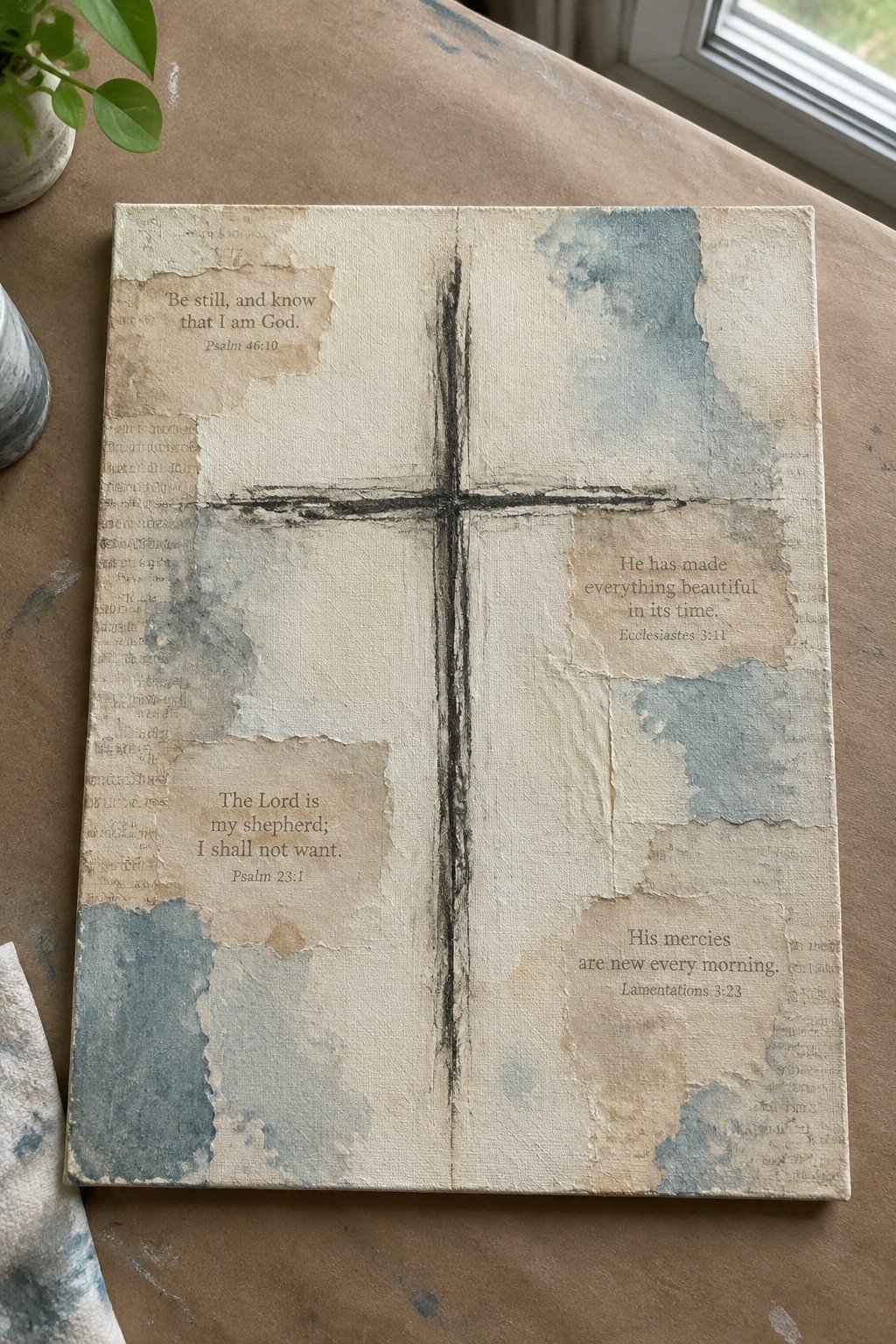 Distressed canvas with black cross, four Bible verses, blue tones on table