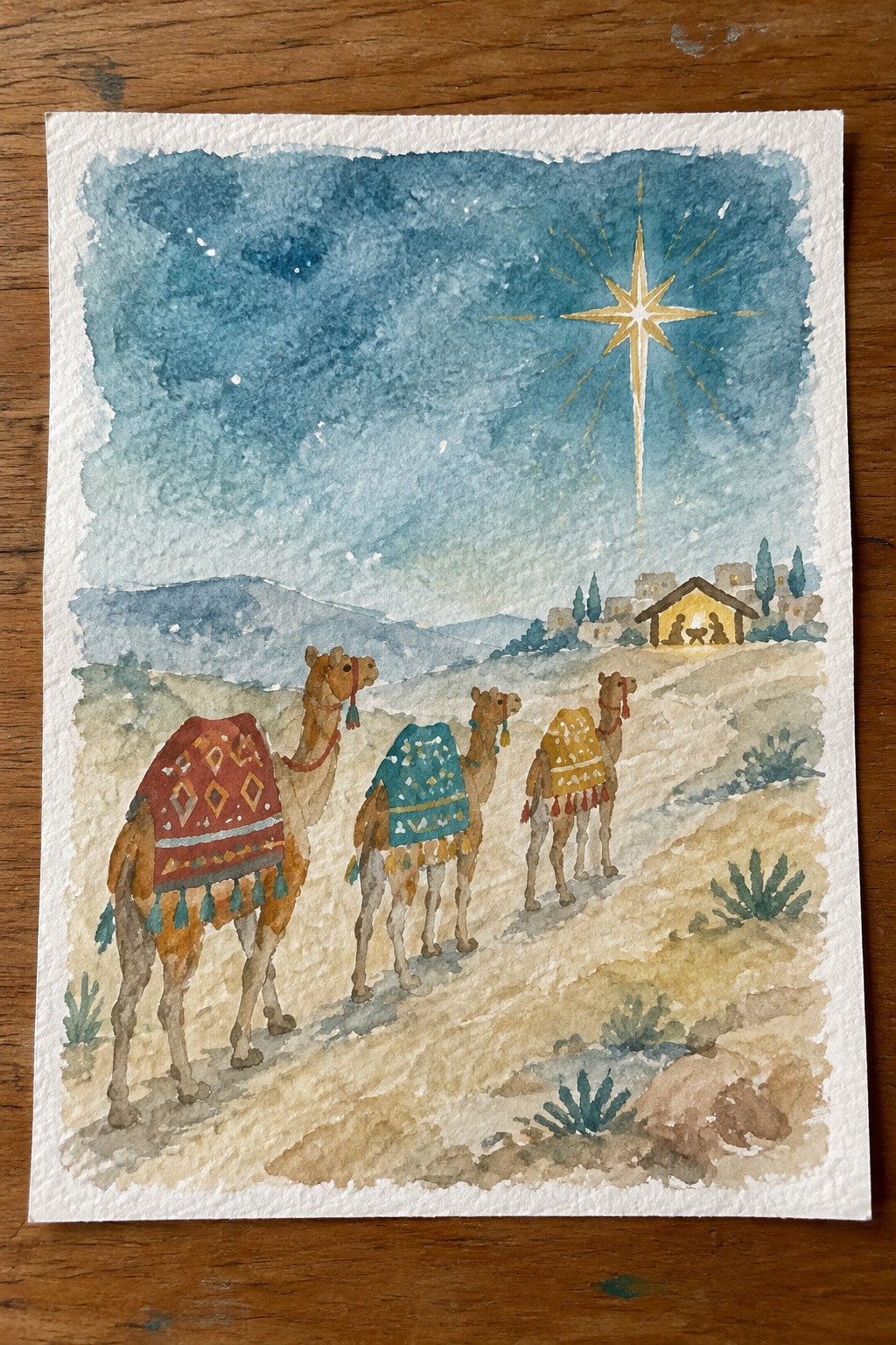 Three watercolor camels with red, teal, and yellow blankets approach a glowing nativity under a bright star.