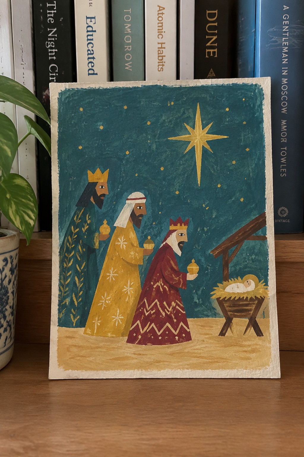 Three kings in ornate teal, yellow, and red robes approach a manger under a golden star.