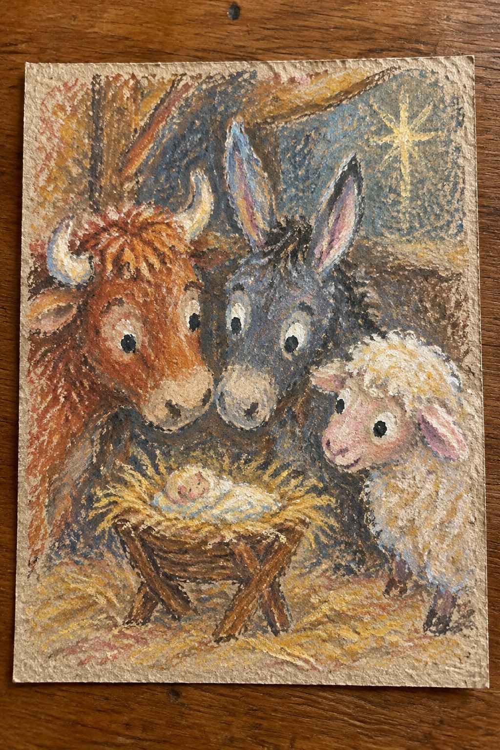 A painting shows a baby in a manger with a brown cow, gray donkey, and white sheep gathered closely around it under a starry sky.