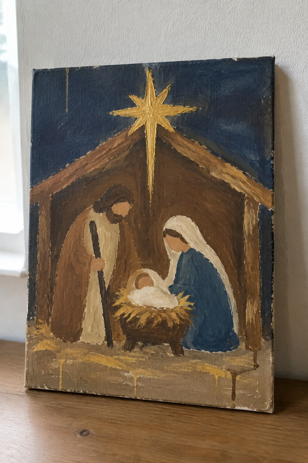 Nativity painting: Joseph in brown robe with staff, Mary in blue veil, baby in straw manger under golden star.