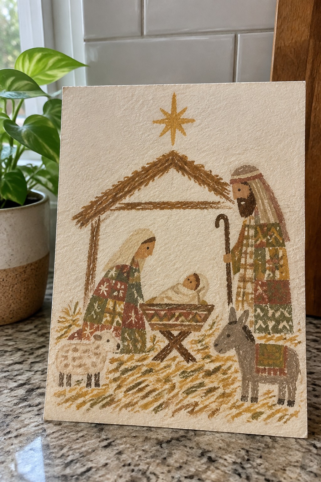 Folk-art watercolor nativity with patterned robes, manger, star, sheep and donkey by stable.