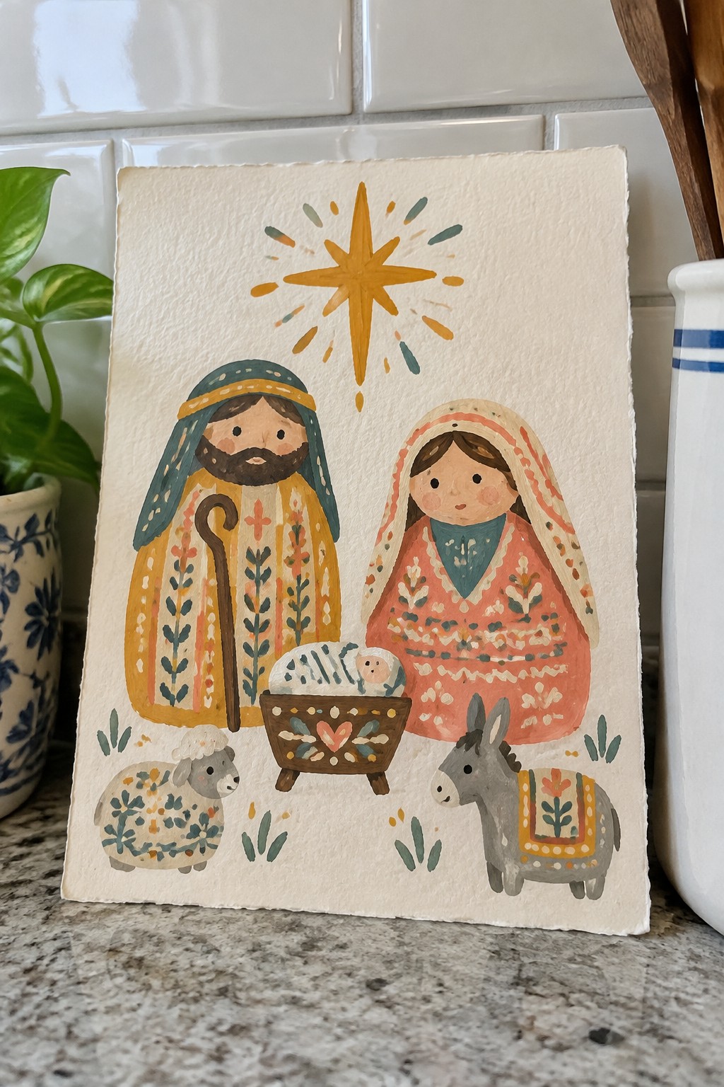 Watercolor folk nativity with patterned Joseph, veiled Mary, manger, star, sheep, and donkey.