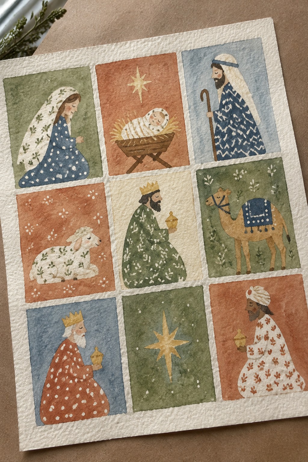 A 3x3 grid of watercolor illustrations showing nine separate Nativity figures and symbols including Mary, baby Jesus in a manger, Joseph, a sheep, three wise men, a camel, and two stars.