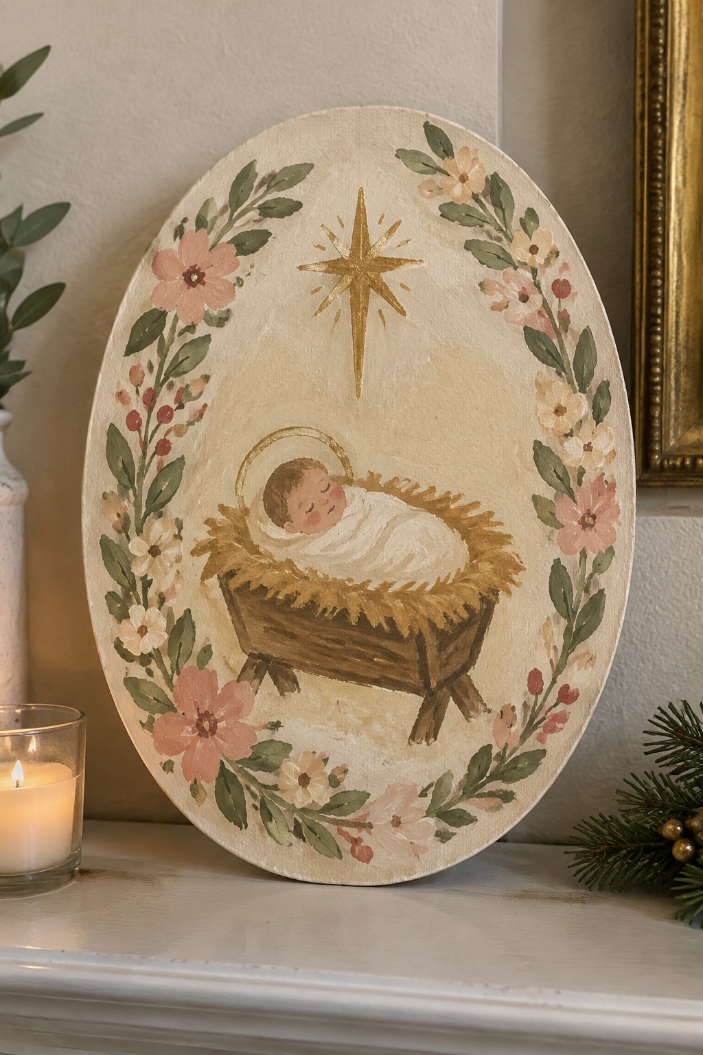 Oval canvas nativity painting of baby in manger under gold star with pink floral wreath.