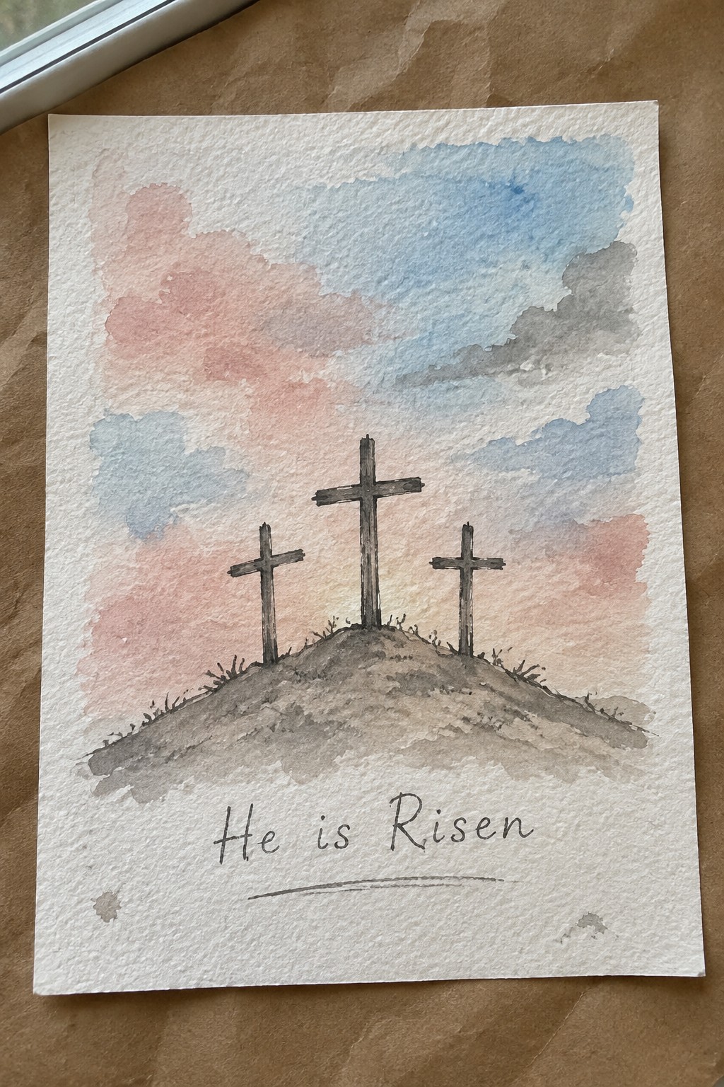 Watercolor painting of three crosses on a hill with a pink and blue sky and the text 