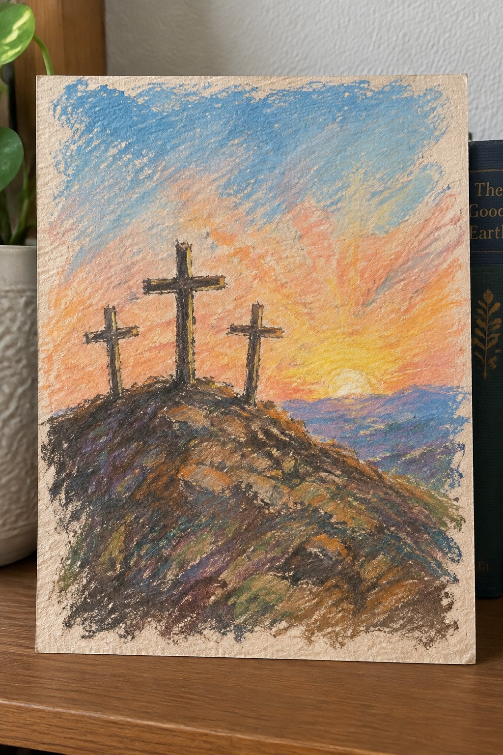 Three crosses on a hill under a vivid orange-blue sunset sky in pastel art.