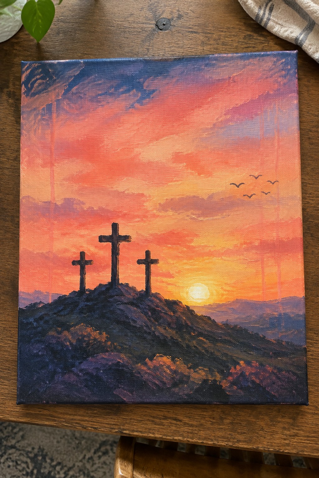 Three crosses on a hill under vibrant orange-pink sunset sky with flying birds.