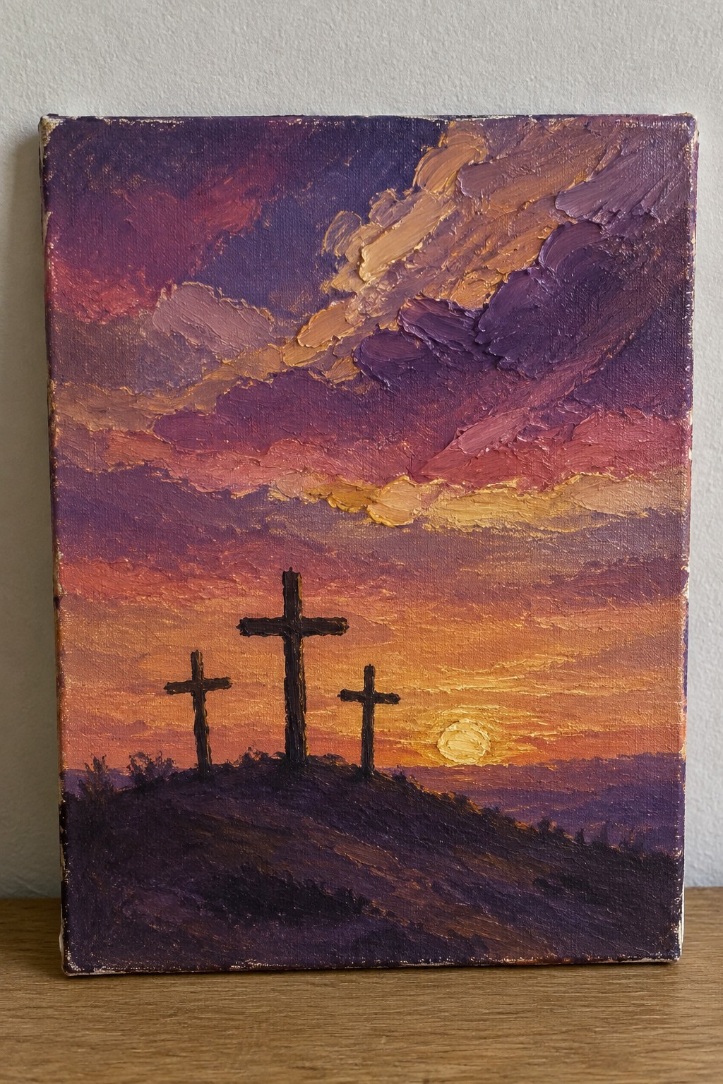Three crosses silhouetted on a hill under thickly textured purple-orange sunset skies