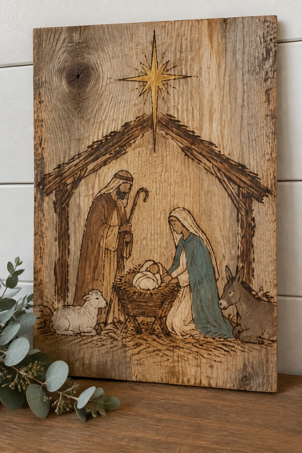 Wood-burned nativity plaque showing Joseph, Mary in blue, manger, sheep, donkey, and golden star.