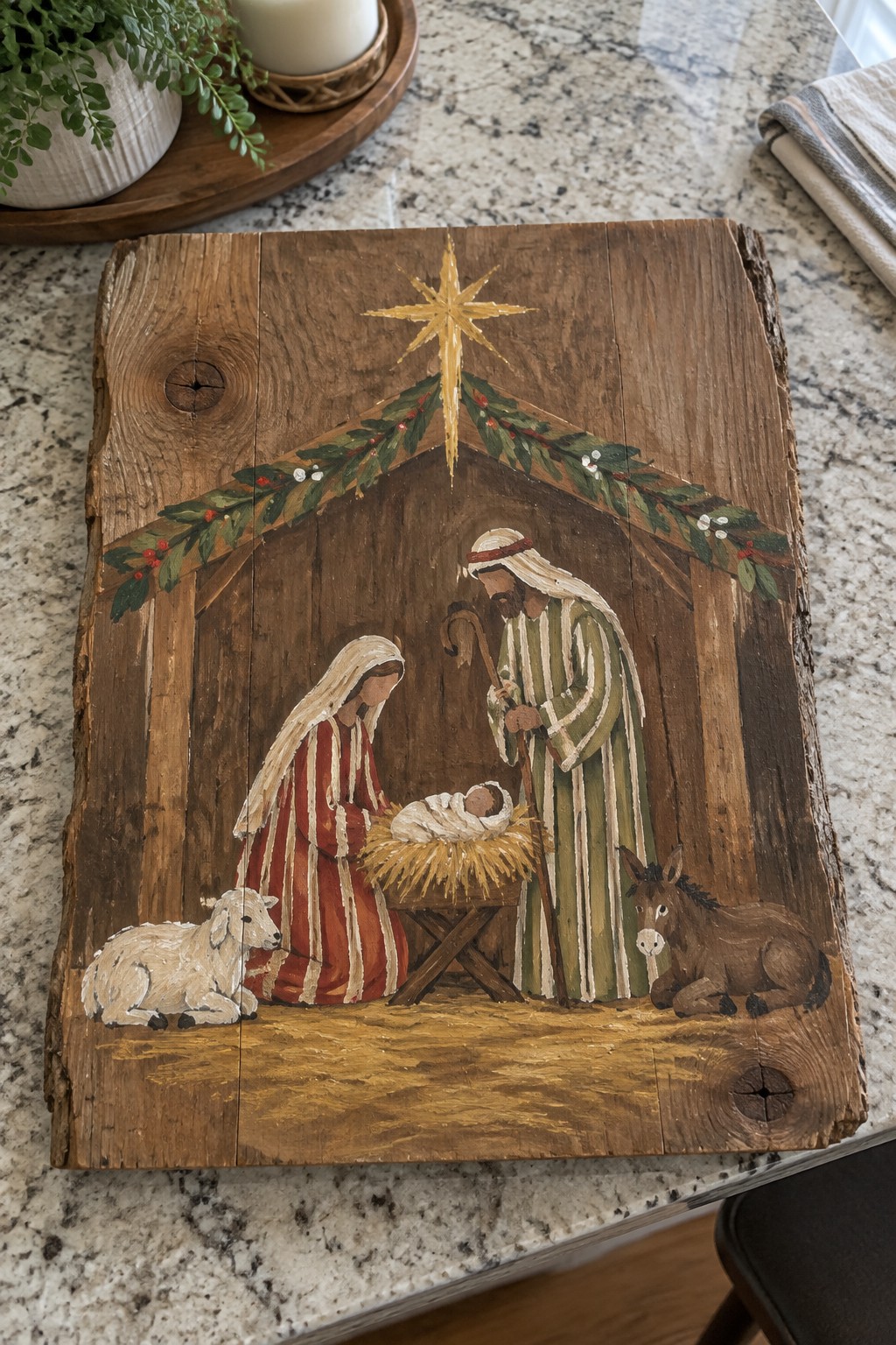 A rustic nativity painting on a wooden panel showing Mary, Joseph, baby Jesus in a manger, a sheep, and a donkey under a star and garland.